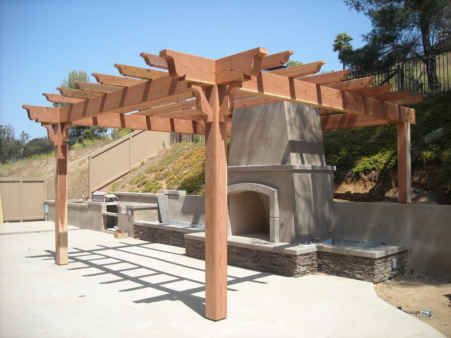 Redwood pergola with stone fireplace outdoor kitchen below it