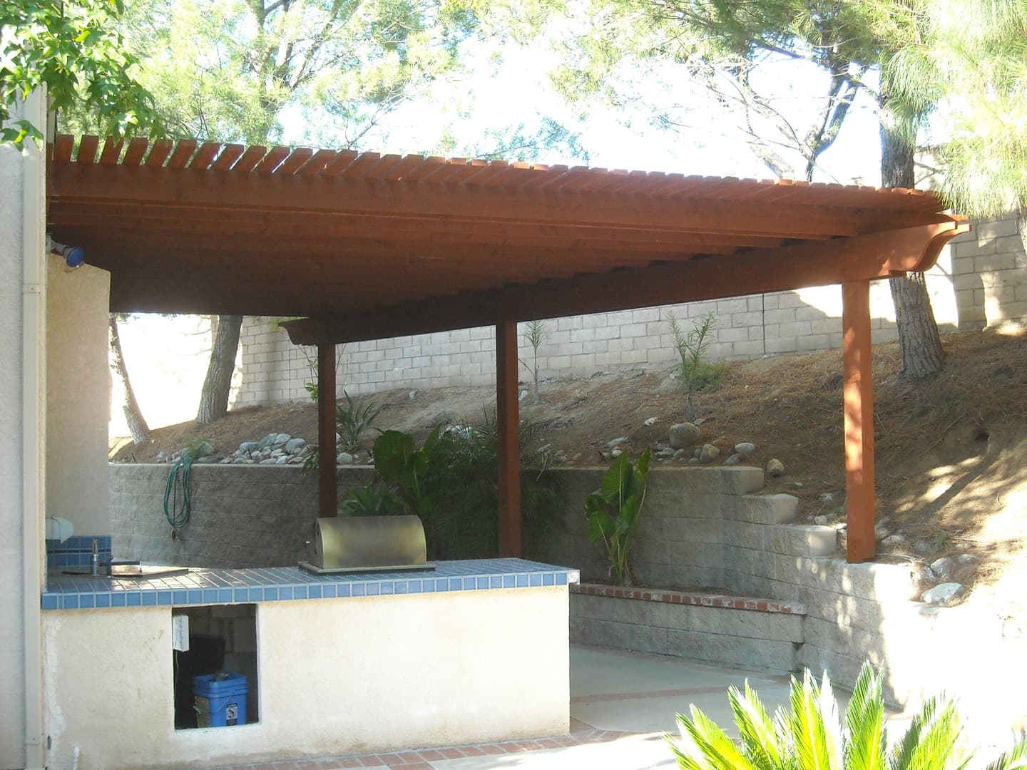 Mahogany-stained pergola sheltering a tiled outdoor counter and grill