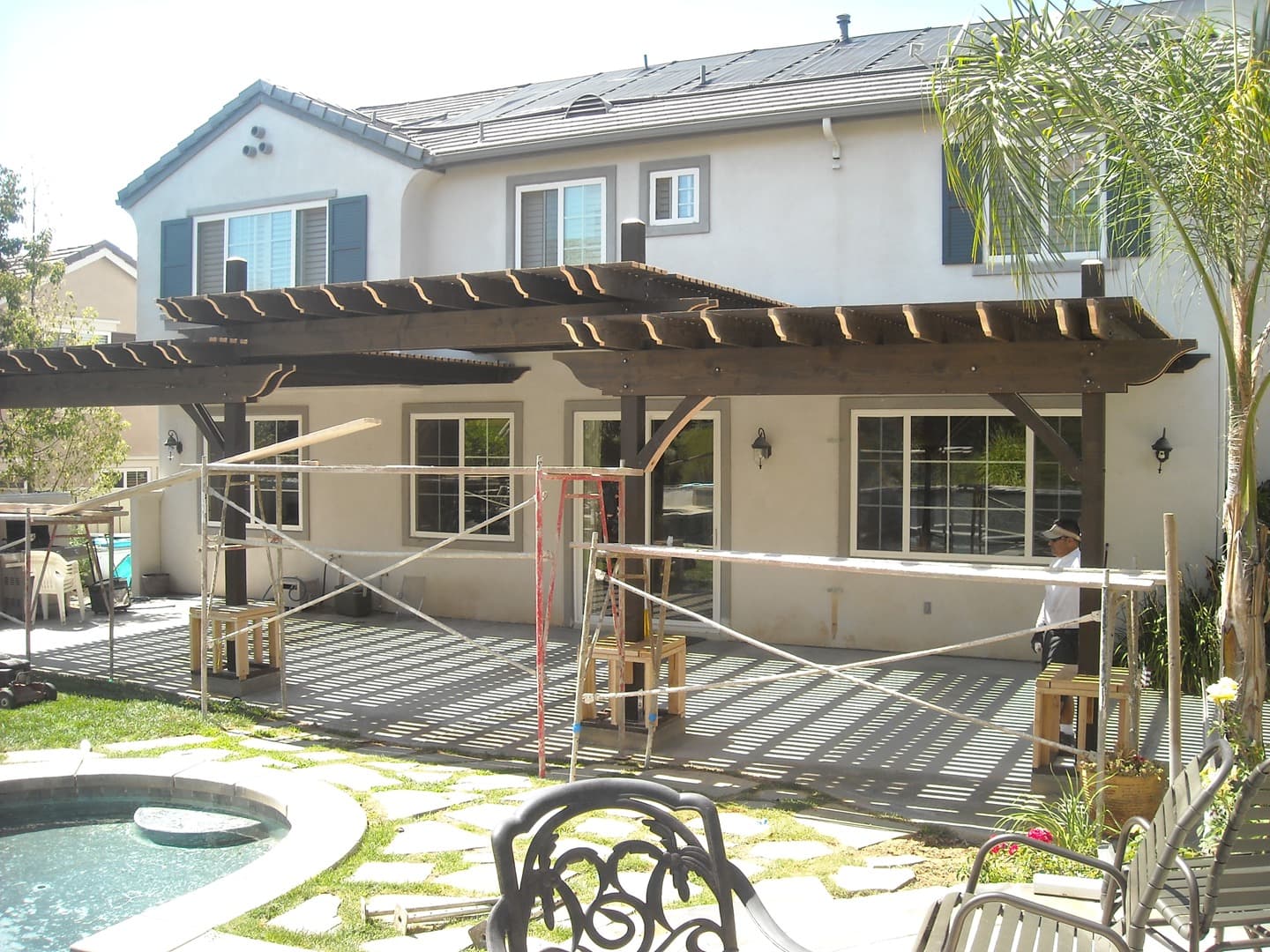 Two-bay espresso-stained pergola against a two-story stucco home